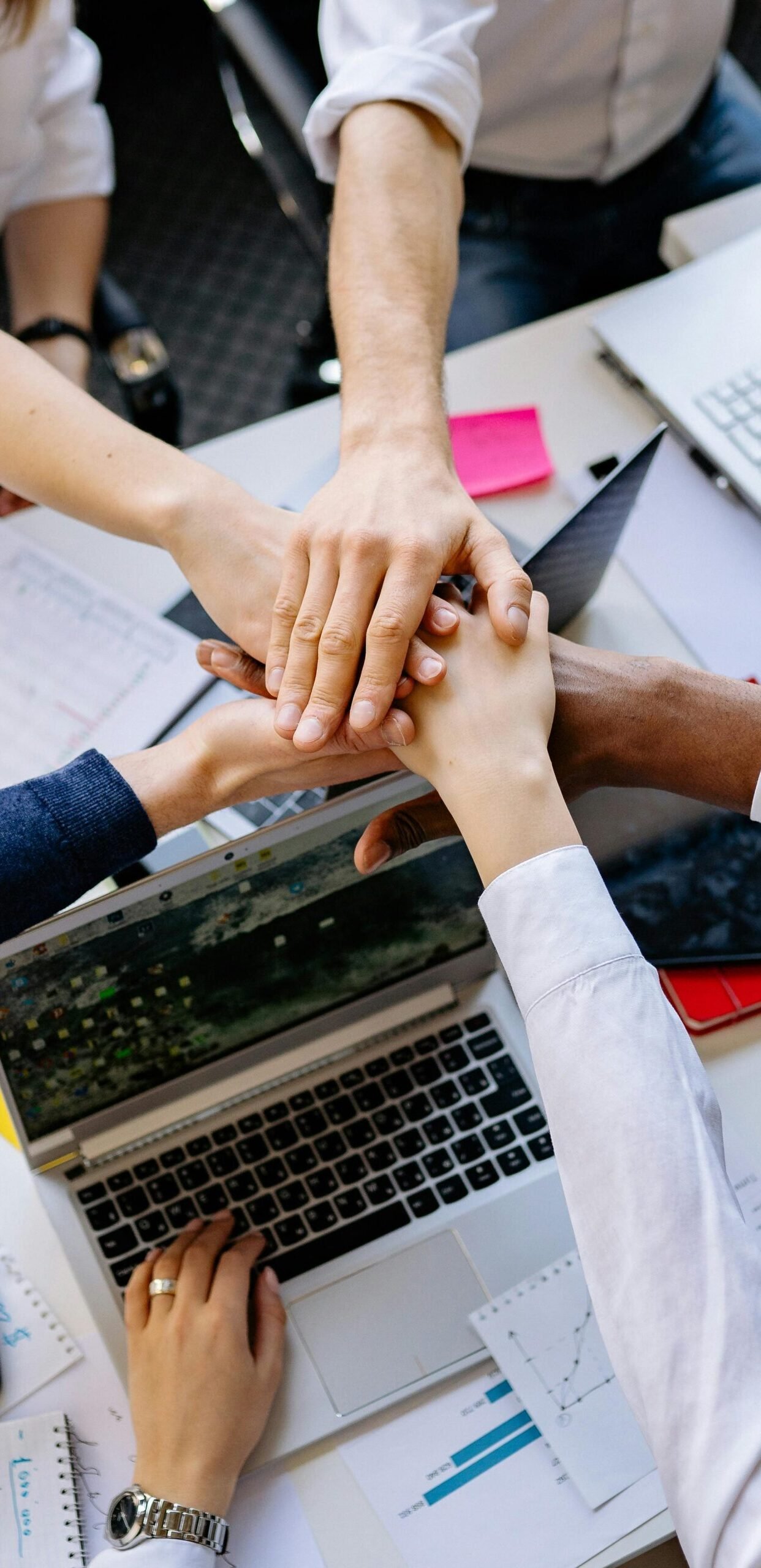 A diverse group of professionals stacking hands over a table symbolizing teamwork and collaboration.